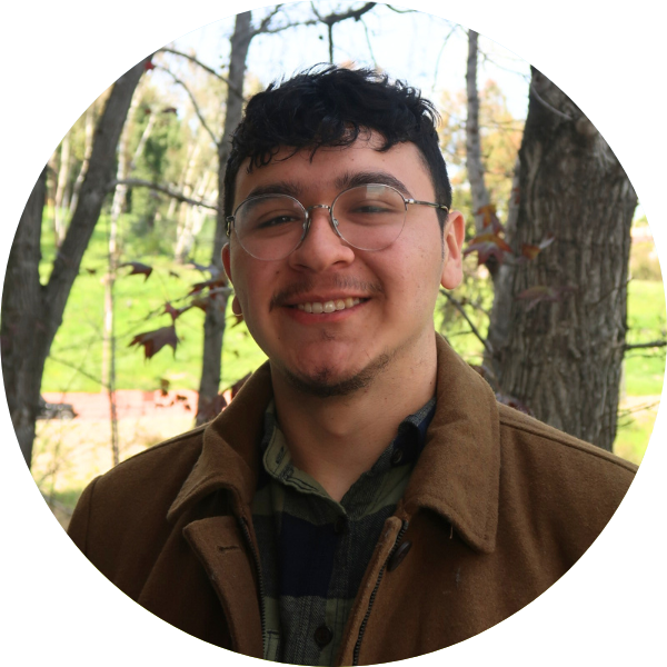 Man smiling with glasses. Trees in the background.