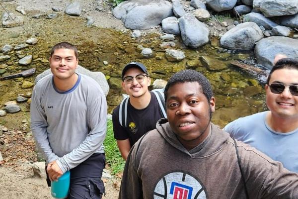 5 Men smiling in front of a stream of water and boulders.